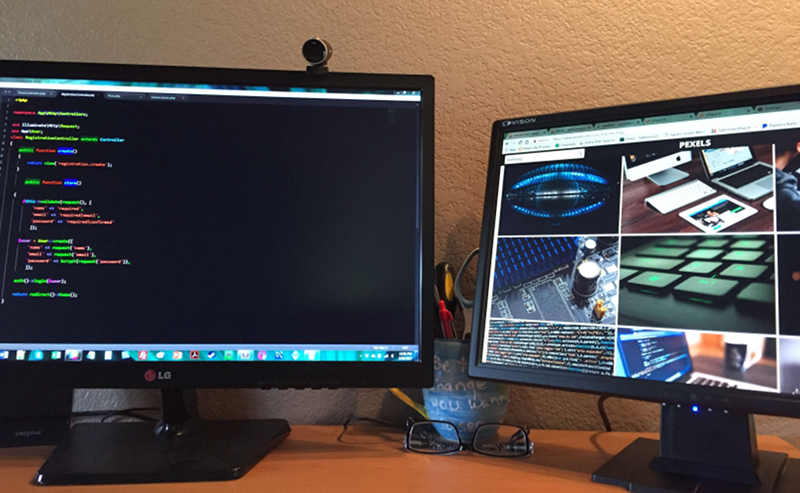 Two monitors on a desk, one showing source code